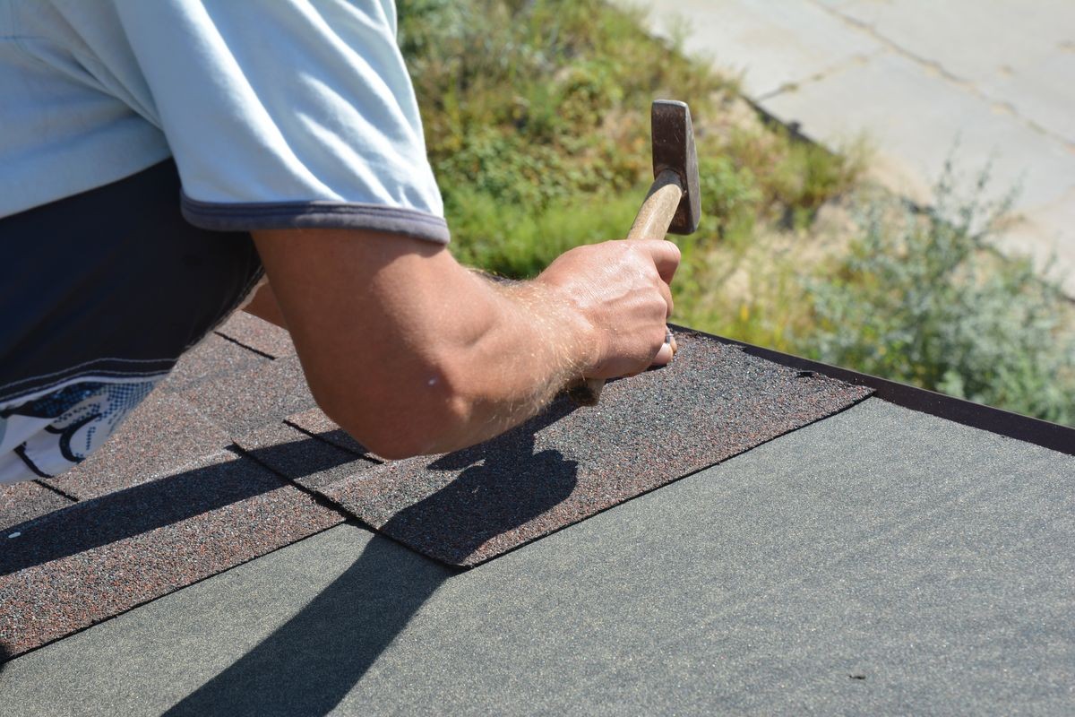 Roofer installing Asphalt Shingles on house Roofing Construction roof corner with hammer and nails. Roofing Construction. Roofing Contractor install Asphalt Shingles roof tiles.