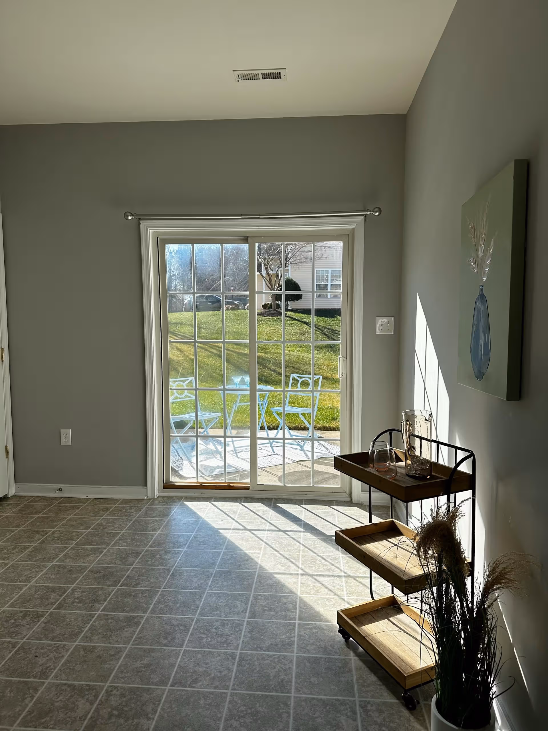 Sunlight shines through glass sliding door onto tiled floor and a small serving cart with a plant nearby.